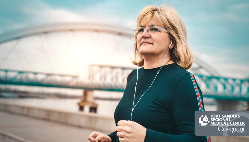 A woman wearing glasses and earphones stands outside near a river and bridge, possibly on a walk or jog as part of her bariatric wellness journey. Sunlight shines in the background. Logos for Fort Sanders Regional Medical Center and Covenant Health are visible.
