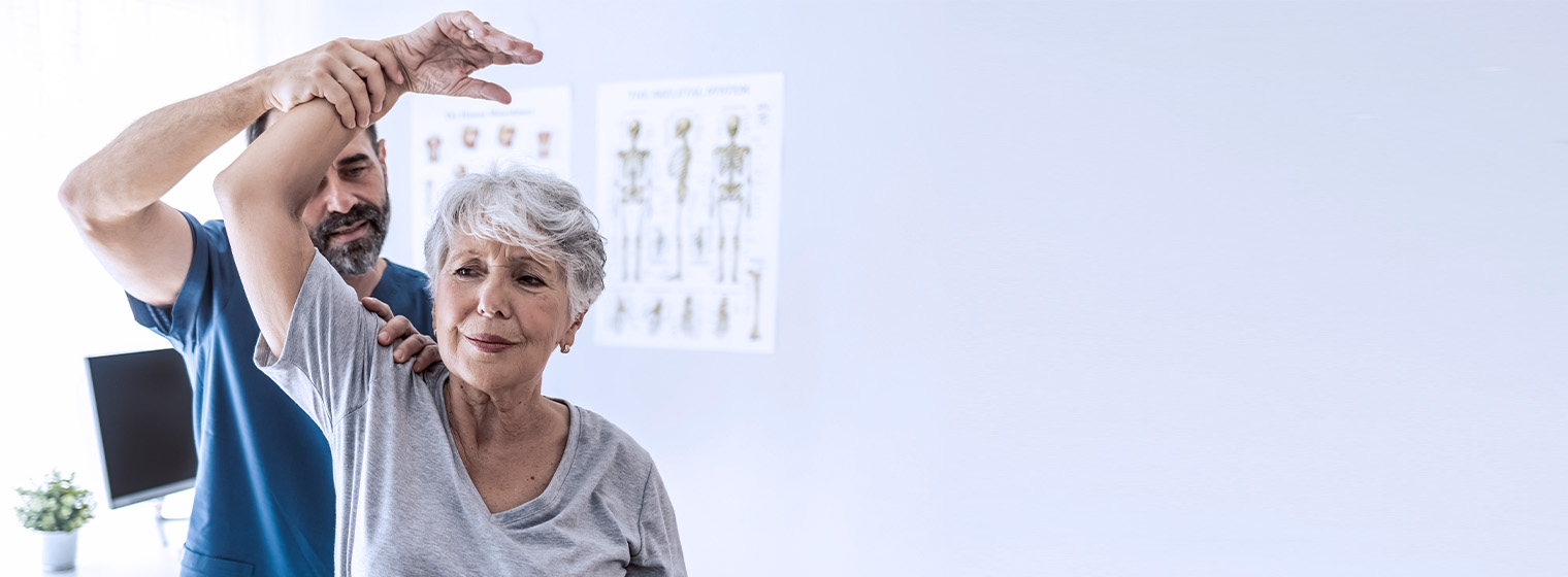 middle age male physical therapist helps elderly female patient lift arm above her head in physical therapy