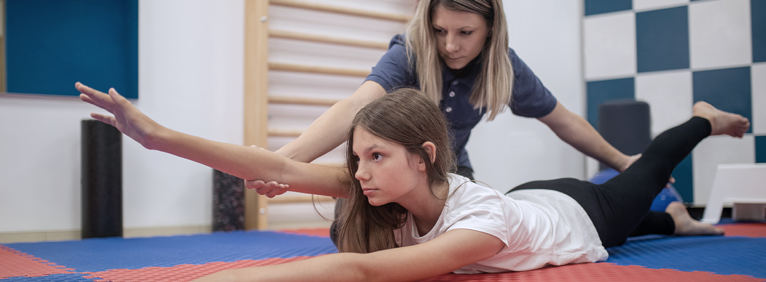 female child laying on a mat stretching with help from female physical therapist