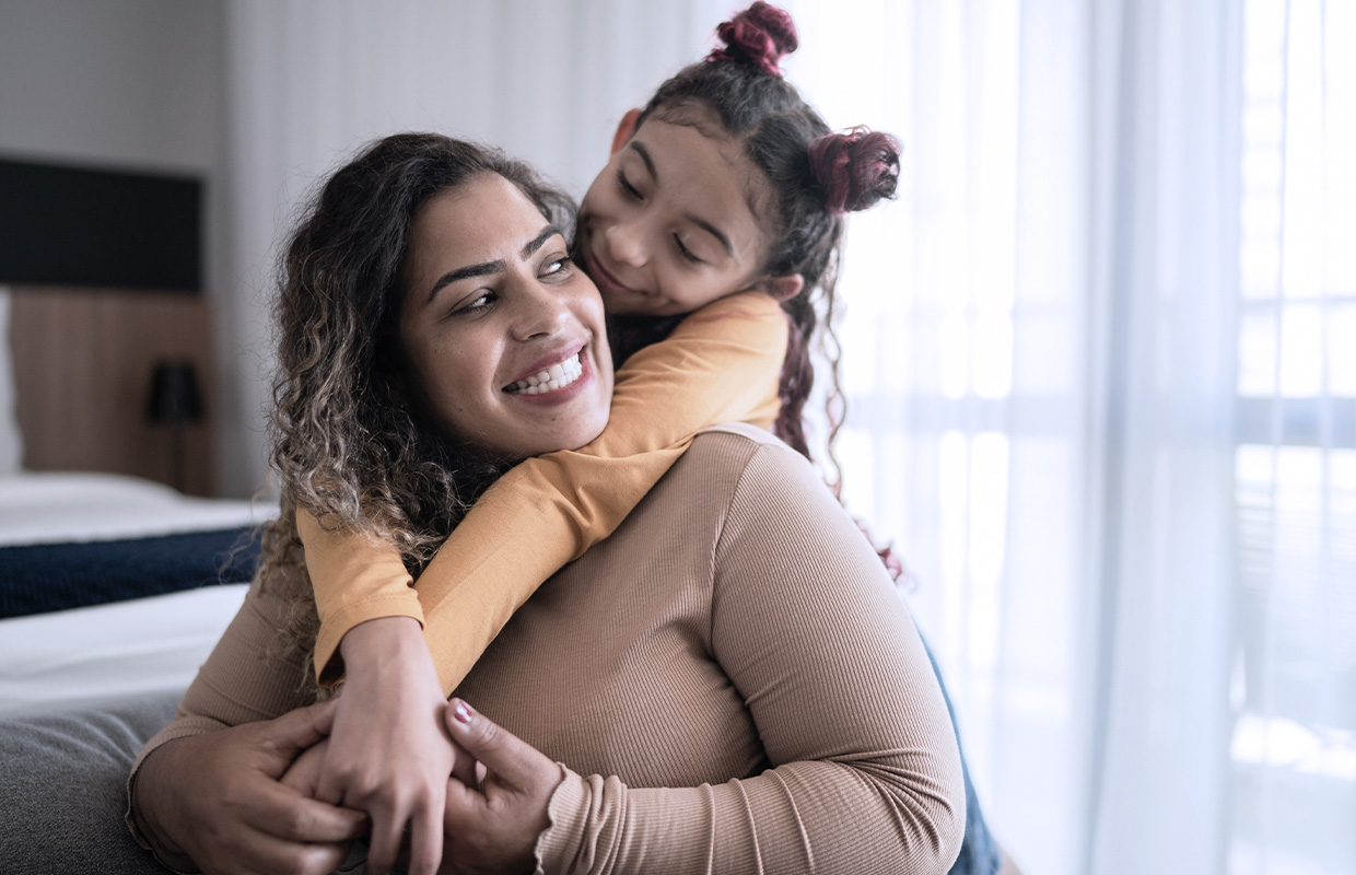 mother smiling with young daughter holding onto her from her back