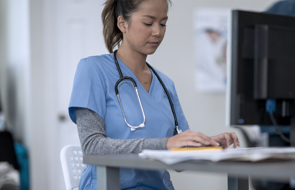nurse in scrubs with stethoscope typing on computer