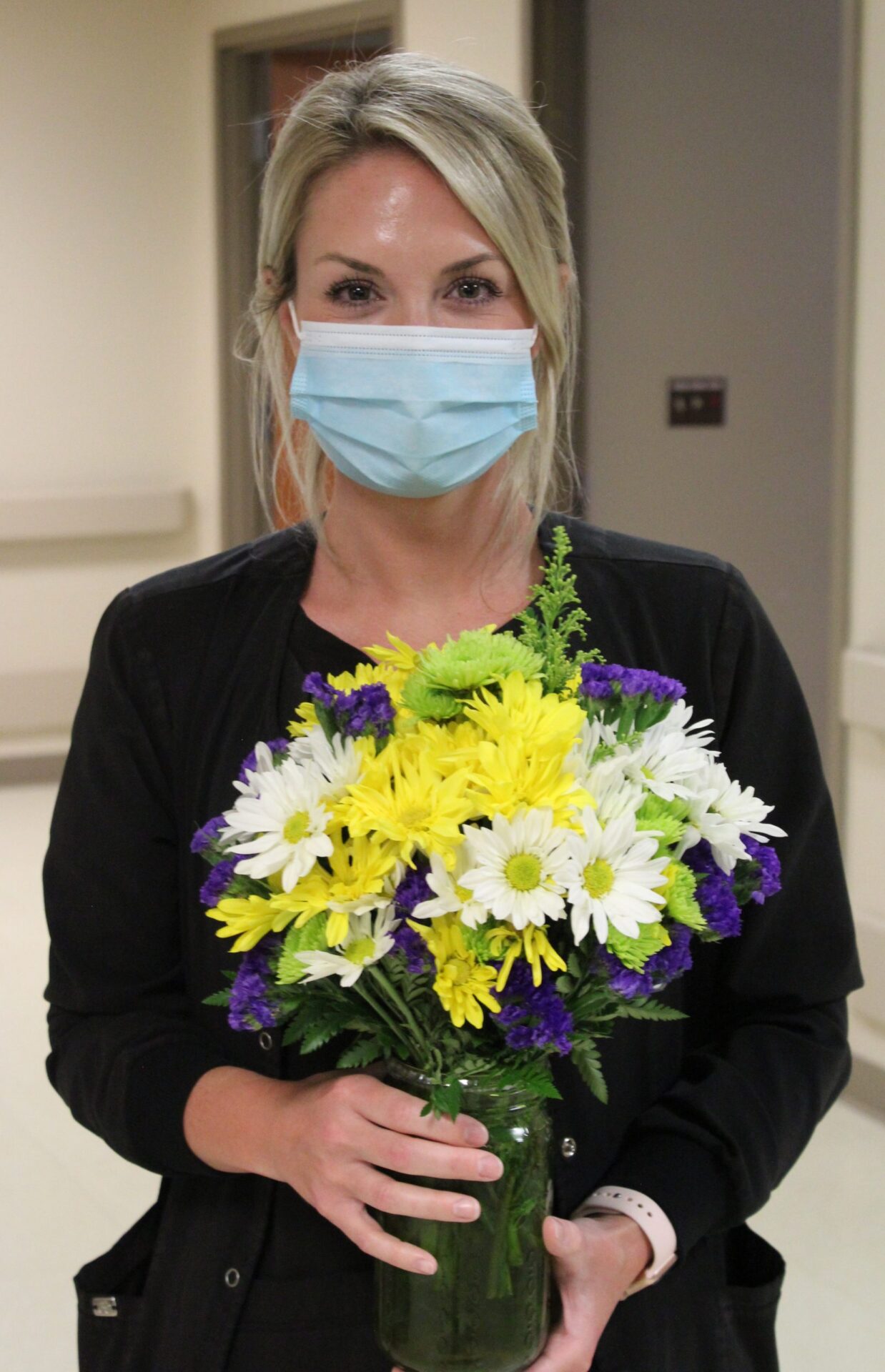 Nurse Laura Ivey dressed in black scrubs holding yellow and white daisies.