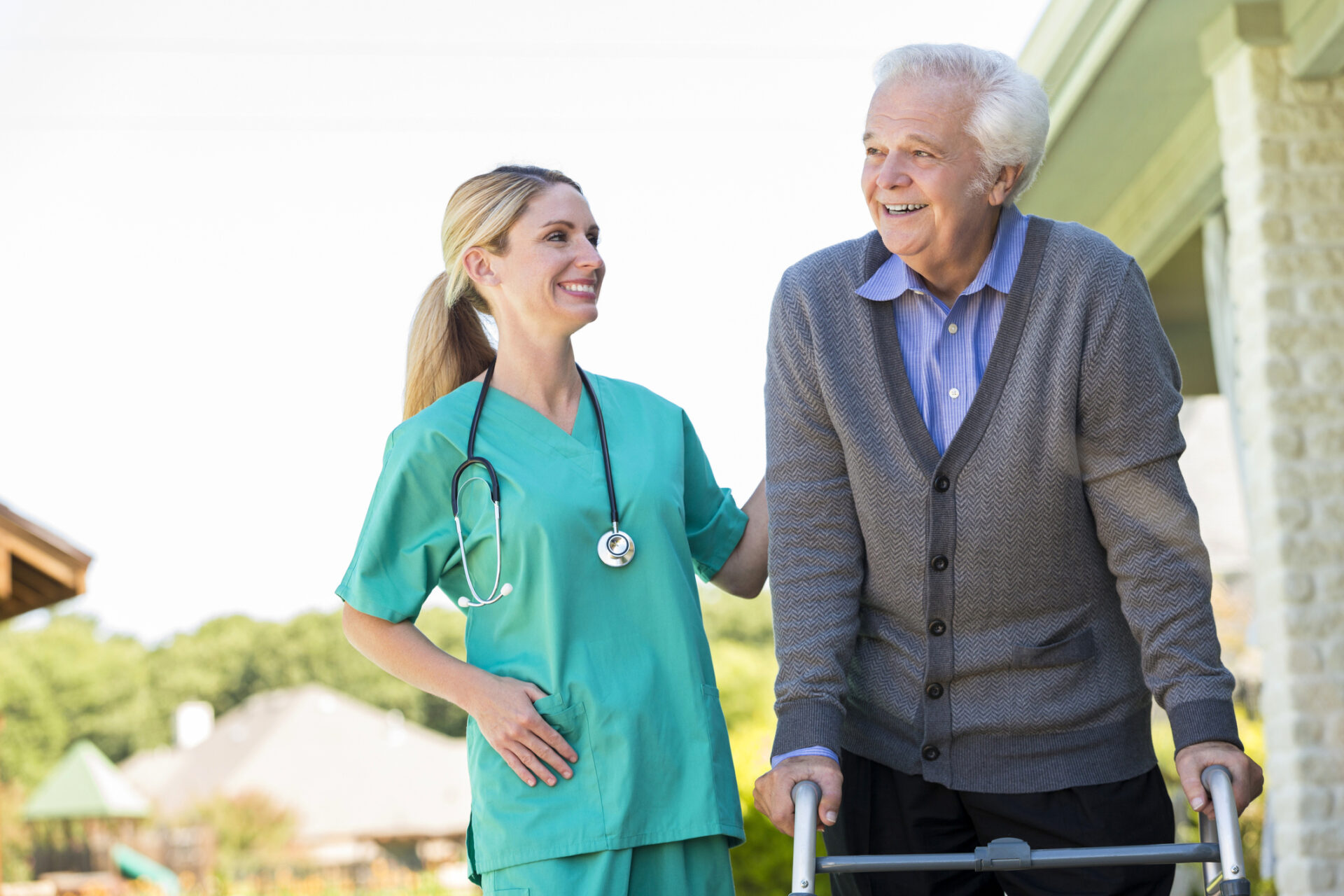 senior man with walker walking outside with help of young female nurse in scrubs