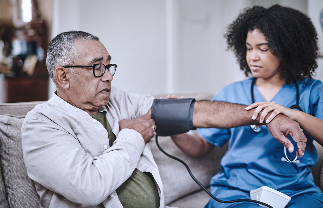 young female nurse taking the blood pressure of an elderly male patient in his home