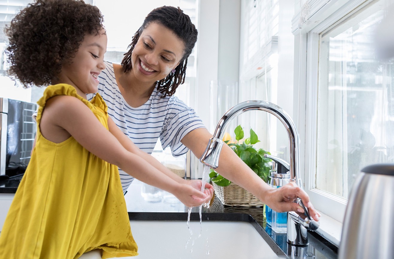 mom and daughter washing hands together at ktichen sink.