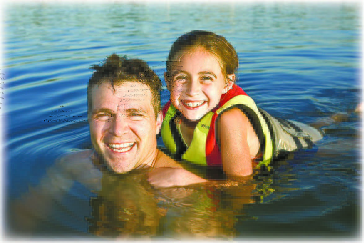 Dad and daughter swimming in water with lifejackets on.