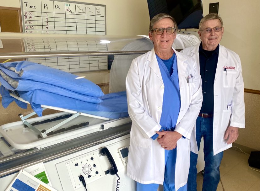 Dr. William Hall and Dr. David Stanley stand in front of a hyperbaric oxygen chamber