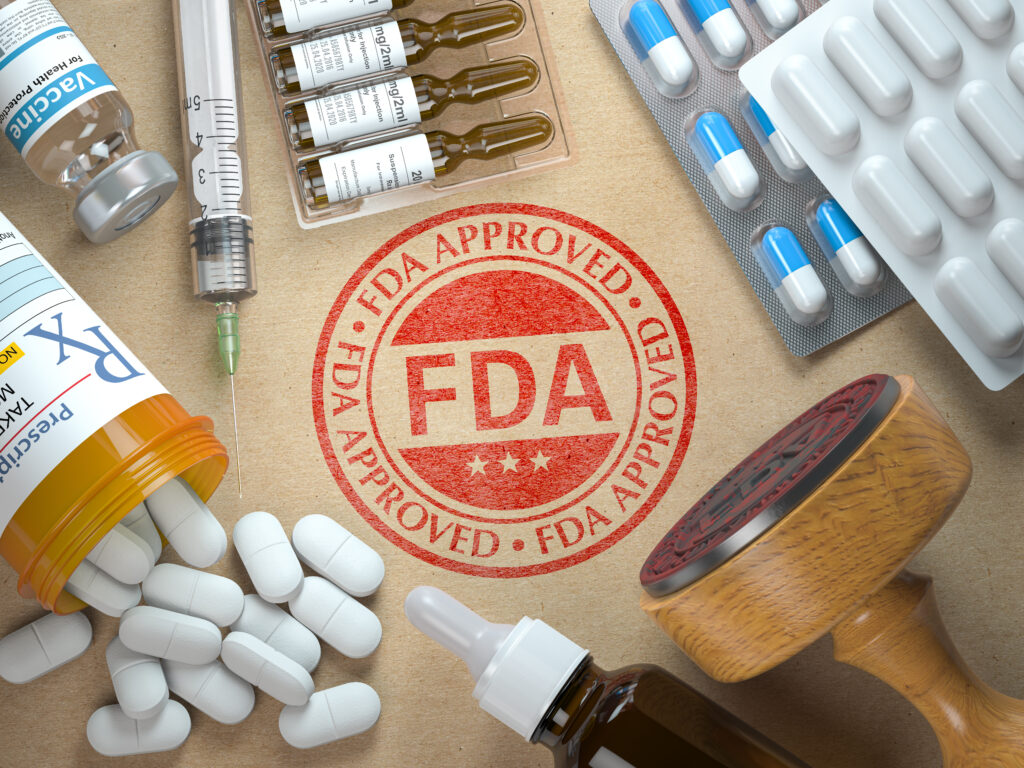 Clinical Trials A red FDA APPROVED stamp is surrounded by various medicines, including pills, capsules, ampoules, a syringe, and prescription bottles—symbolizing treatments that have successfully passed clinical trials phases.