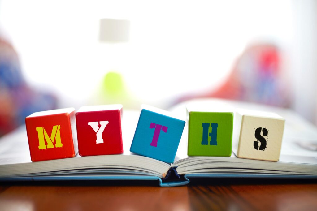 Colorful letter blocks spelling MYTHS are arranged on top of an open book, with a blurred background of various colors.