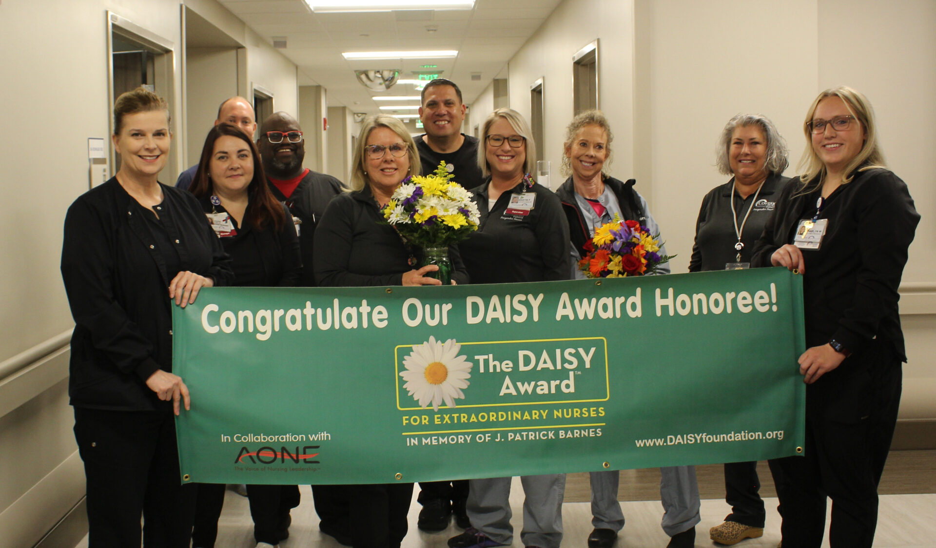 Pamela is pictured leadership team and co-workers holding DAISY banner for photo.