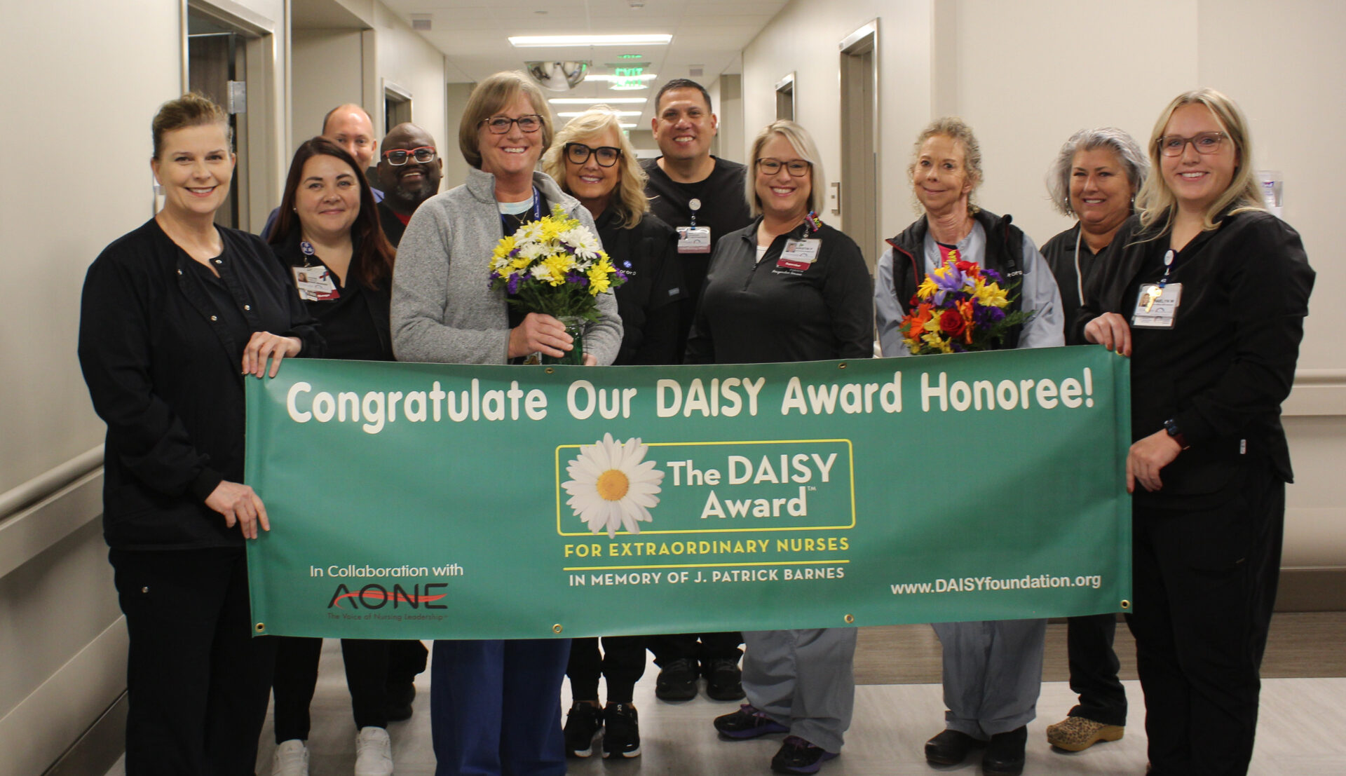 Christy pictured with leadership team and co-workers holding DAISY banner.
