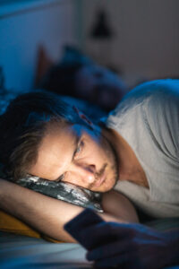 man looks at phone in bed