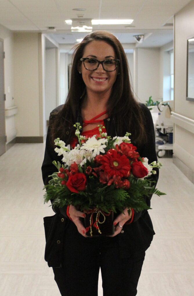 Madison in black scrubs, smiling, holding a daisy arrangement.