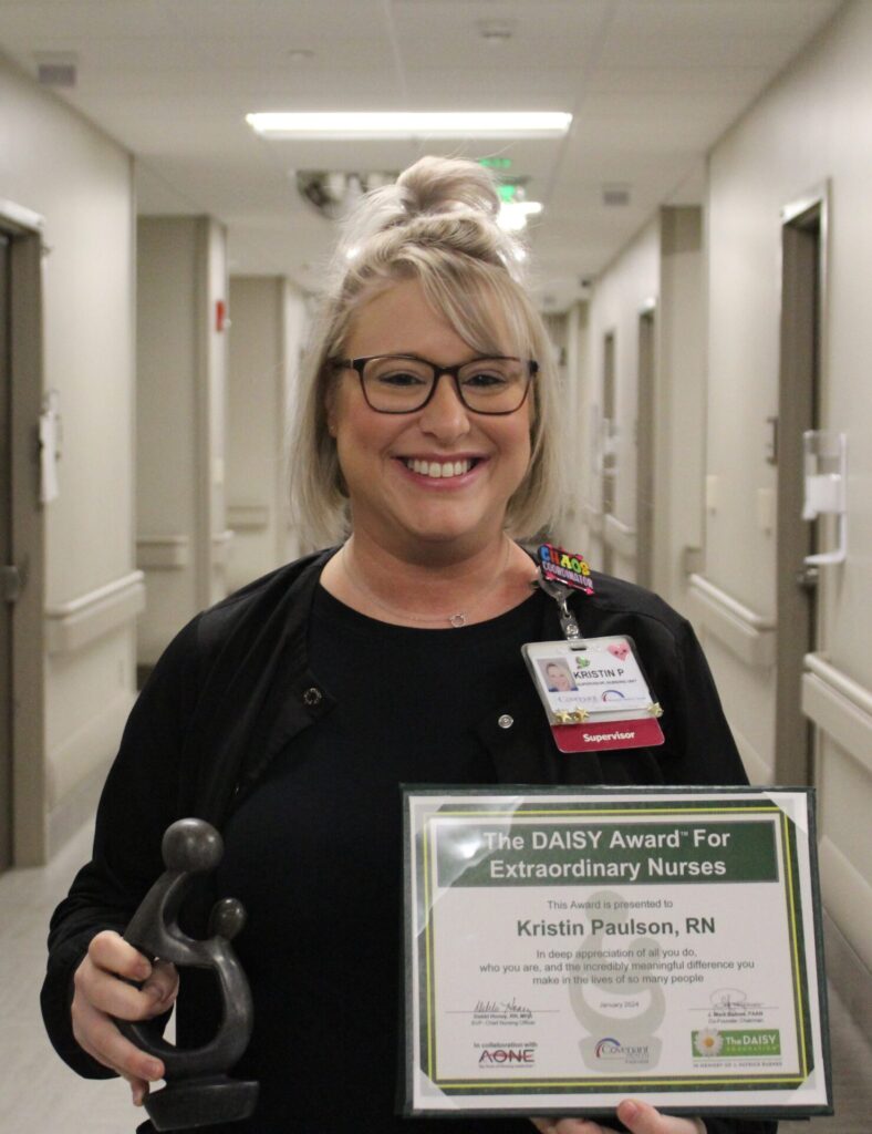 Kristin Paulson smiling in black scrubs, holding sculpture and certificate.