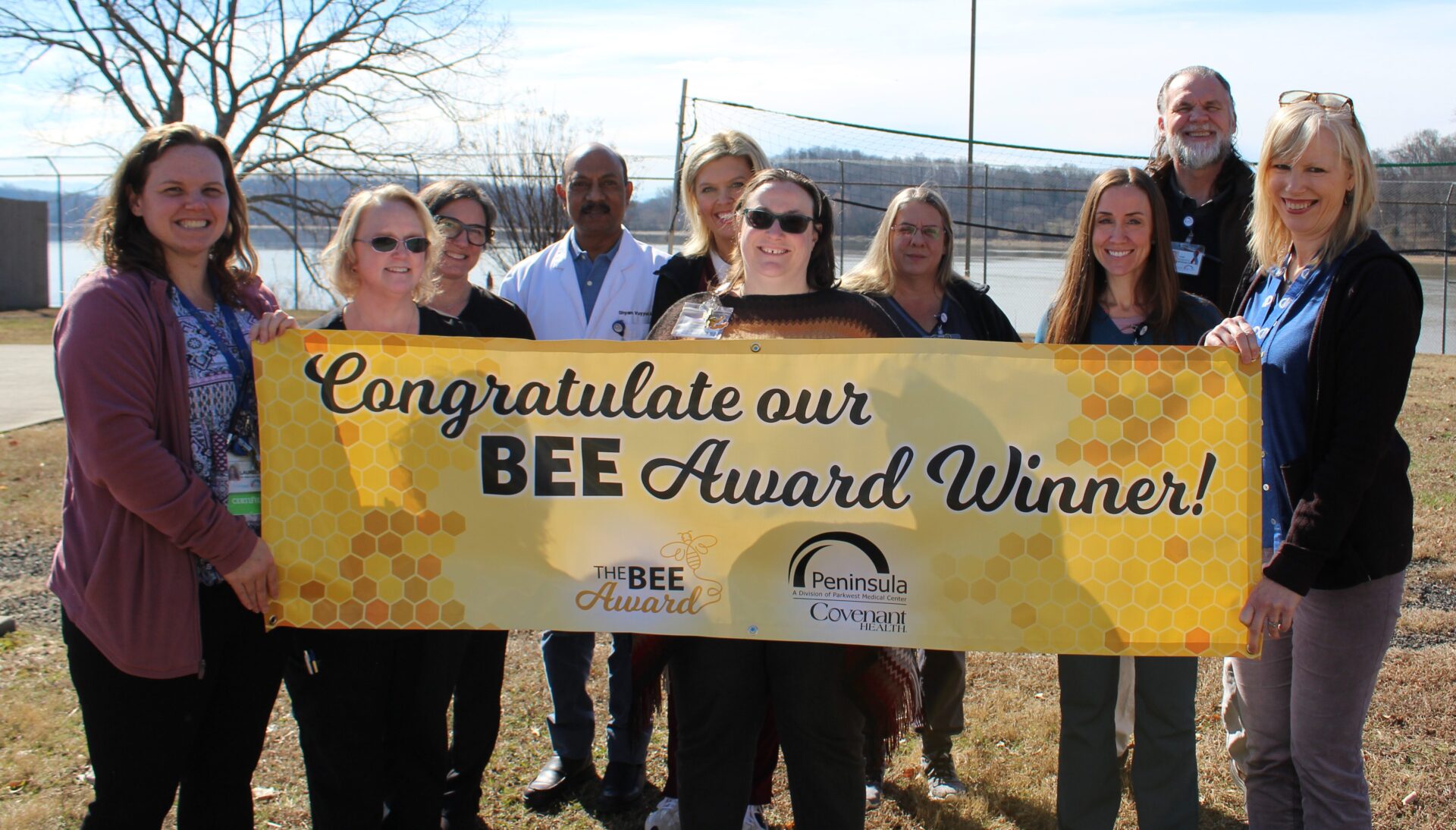 The purpose of image is to celebrate Robin who is pictured in photo. The picture consists of leadership team and Robin holding the BEE banner in front of the water.