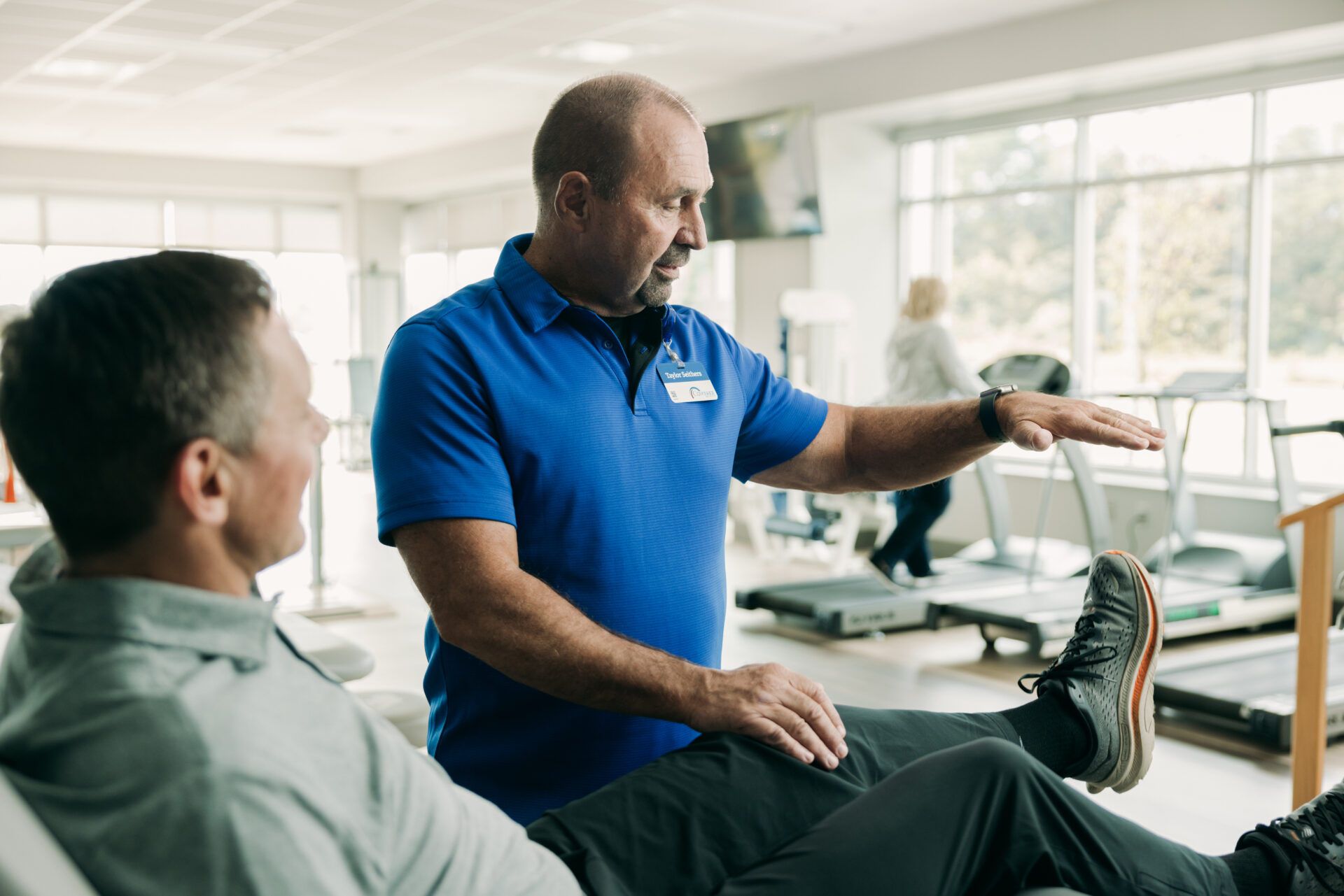 Man doing seated leg lifts with help of rehabilitation therapist