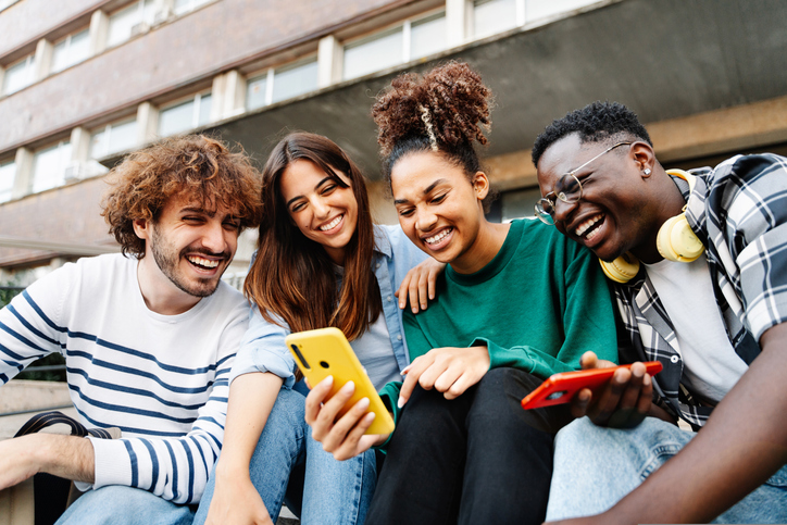 group of young adults outside smiling at a cellphone