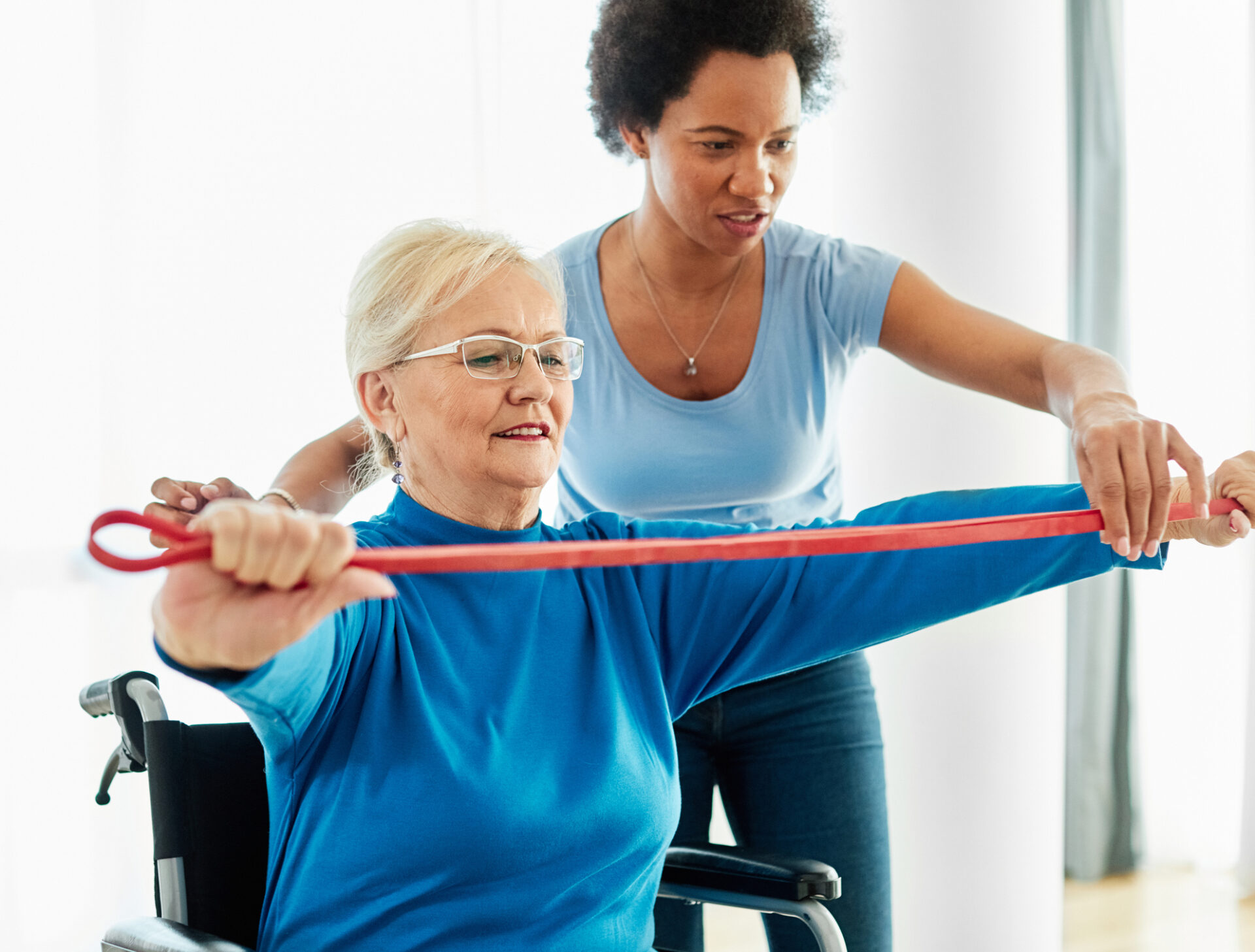 Physical therapist helping woman doing rehabilitation exercise with resistance band