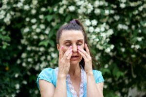 Woman with allergies rubbing eyes near blooming tree
