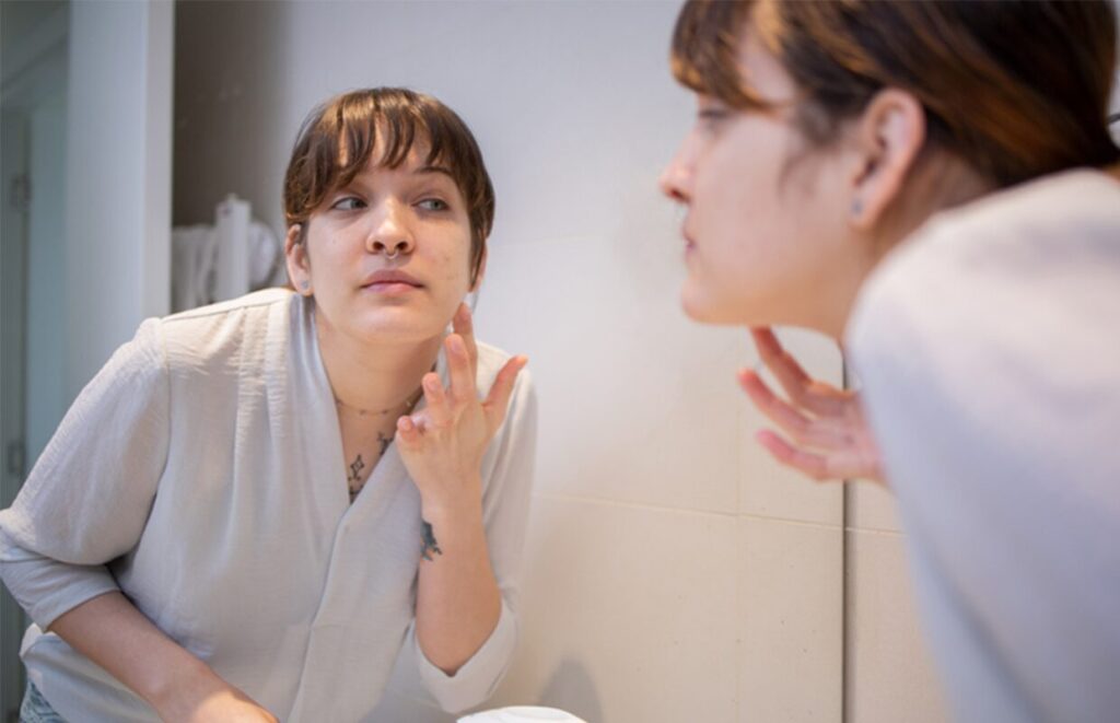 young adult woman putting on face cream in the mirror