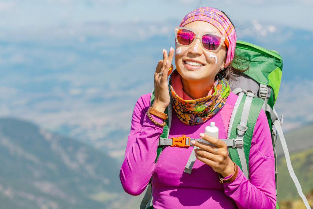 adult woman applying sunscreen to her face while hiking