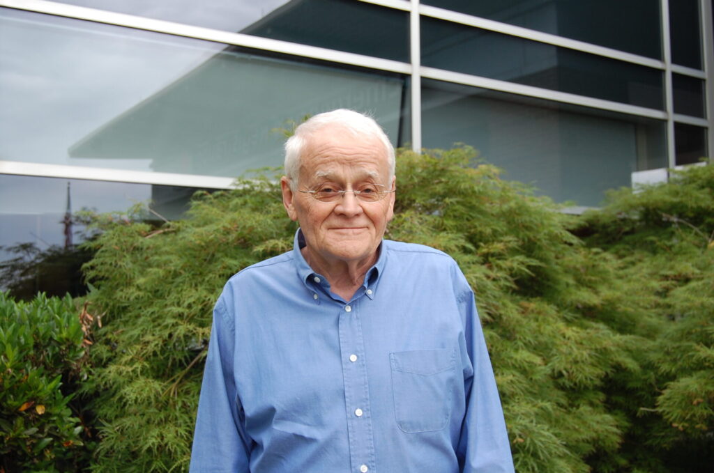 Bill Lockard wearing glasses, blue button up shirt, smiling.