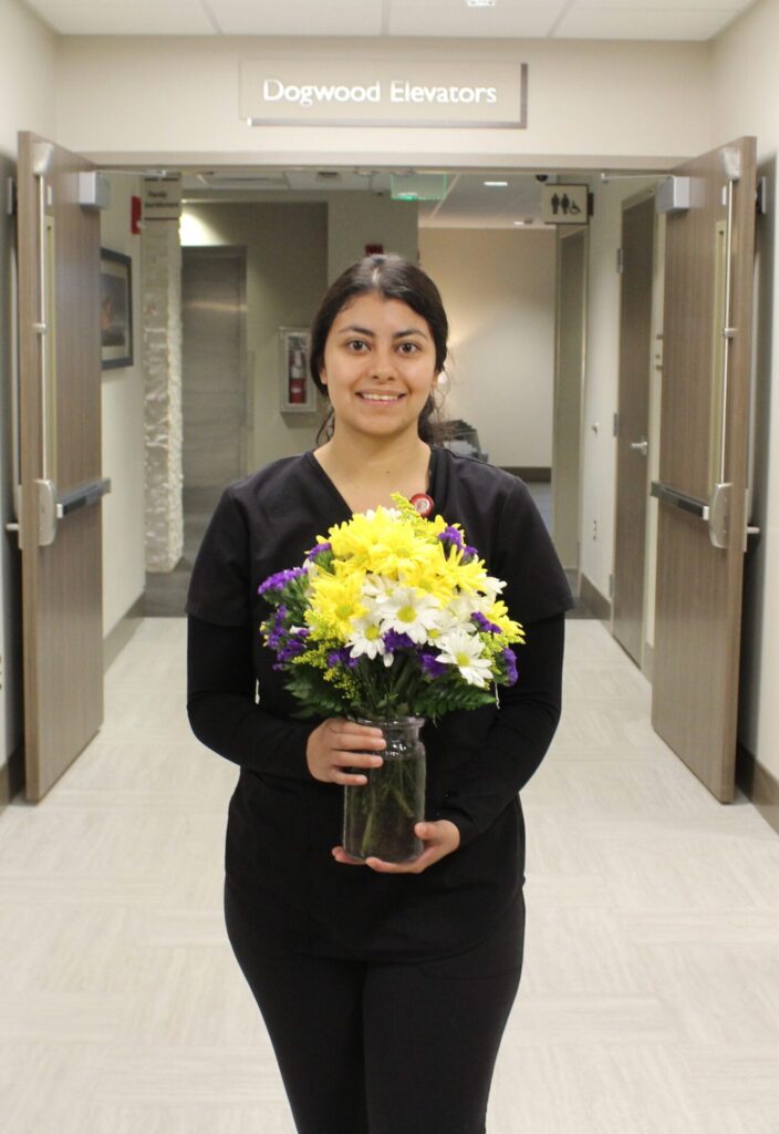 Karina pictured in a hallway holding yellow and white daisies. 