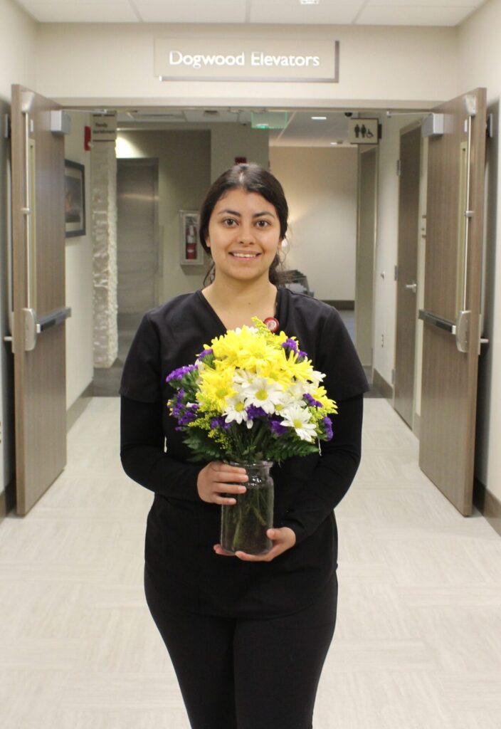 Karina pictured in a hallway holding yellow and white daisies.