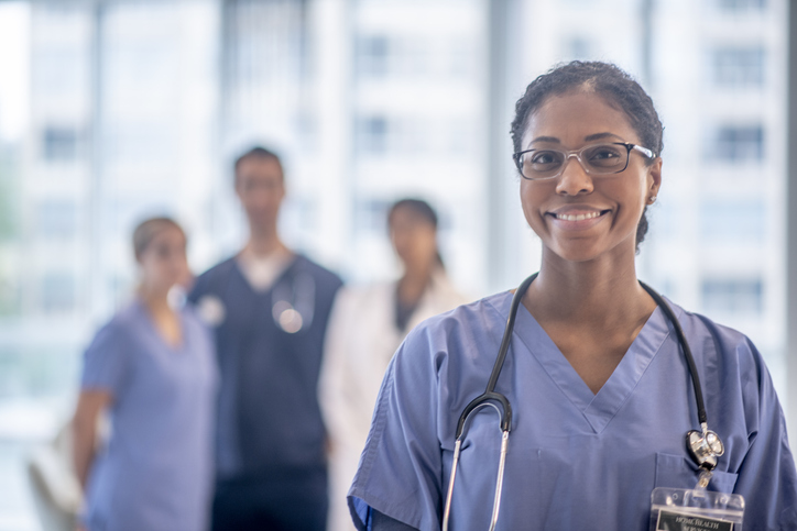 Adult female nurse in scrubs with stethoscope smiling.