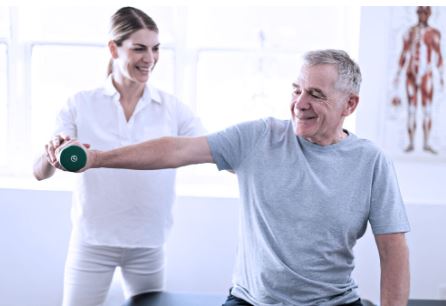 A young female physical therapist helps a senior male patient lift weight.