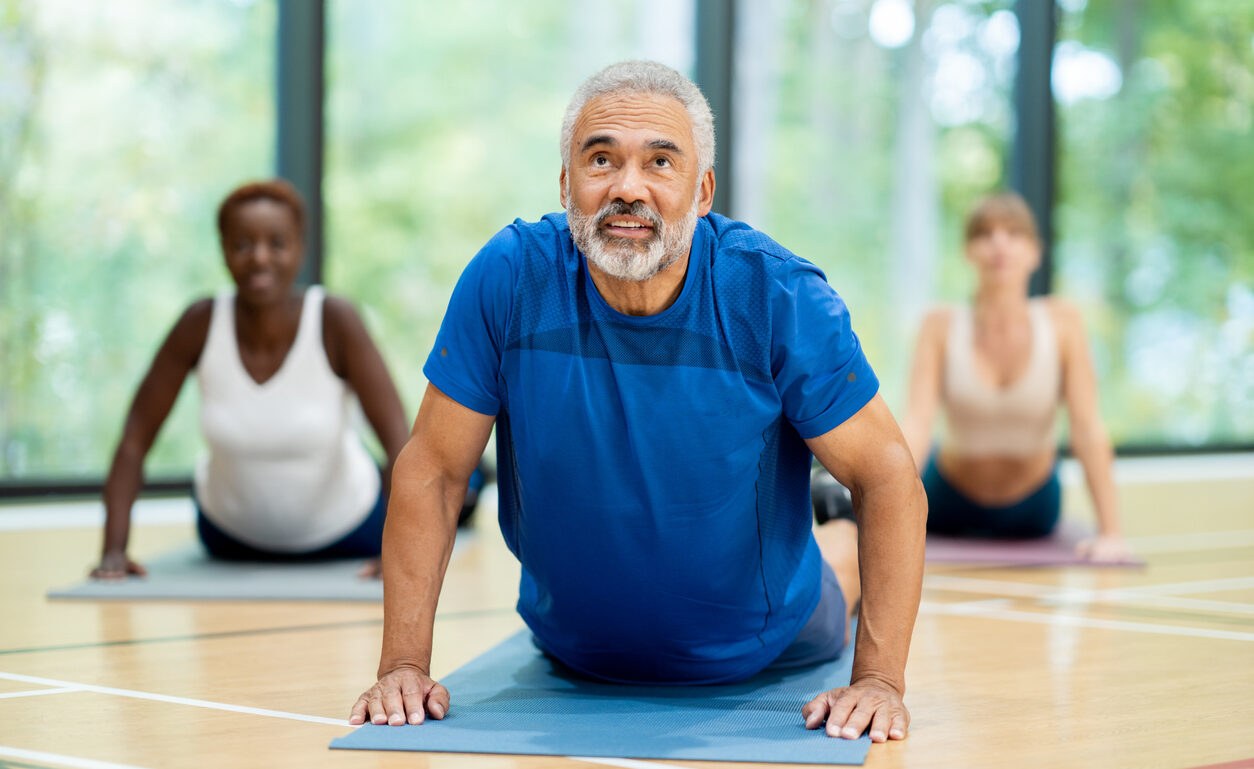 A senior group of adults follows their instructor in an upward dog yoga pose.
