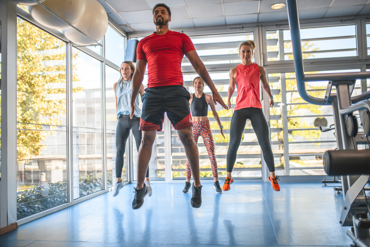 Young men and women doing dynamic jumping exercises at gym.
