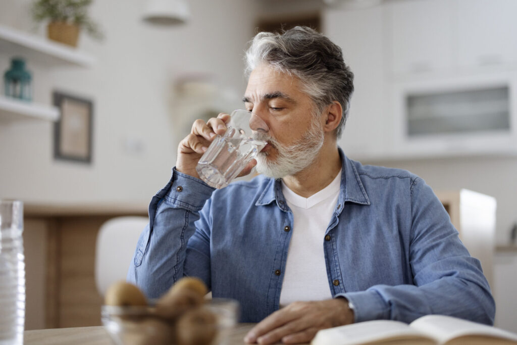 Man at table drinking a glass of water. Rest and fluids are recommended for relief ofmild symptoms of RSV in adults.