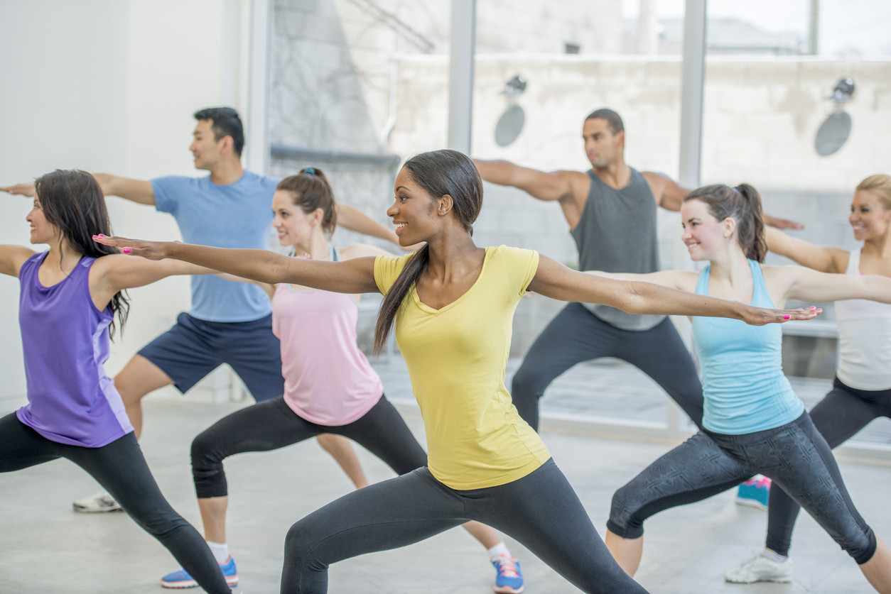 A group of adults hold a warrior two pose in a power yoga class.