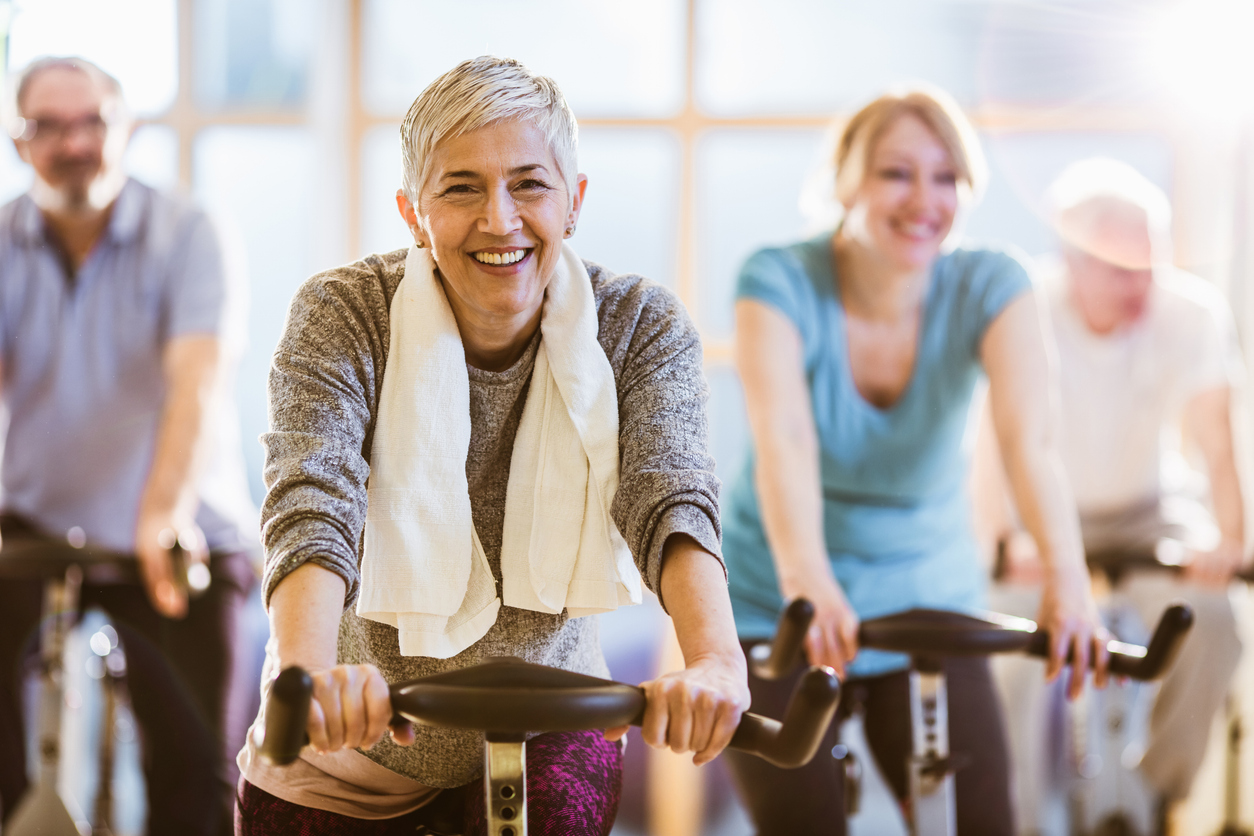 Senior woman smiles as she cycles in a group spin class.
