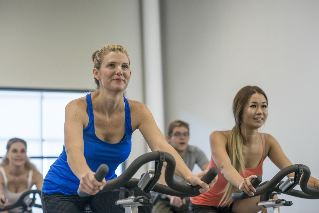 A group of adults exercise together on stationary bicycles in a spin class.