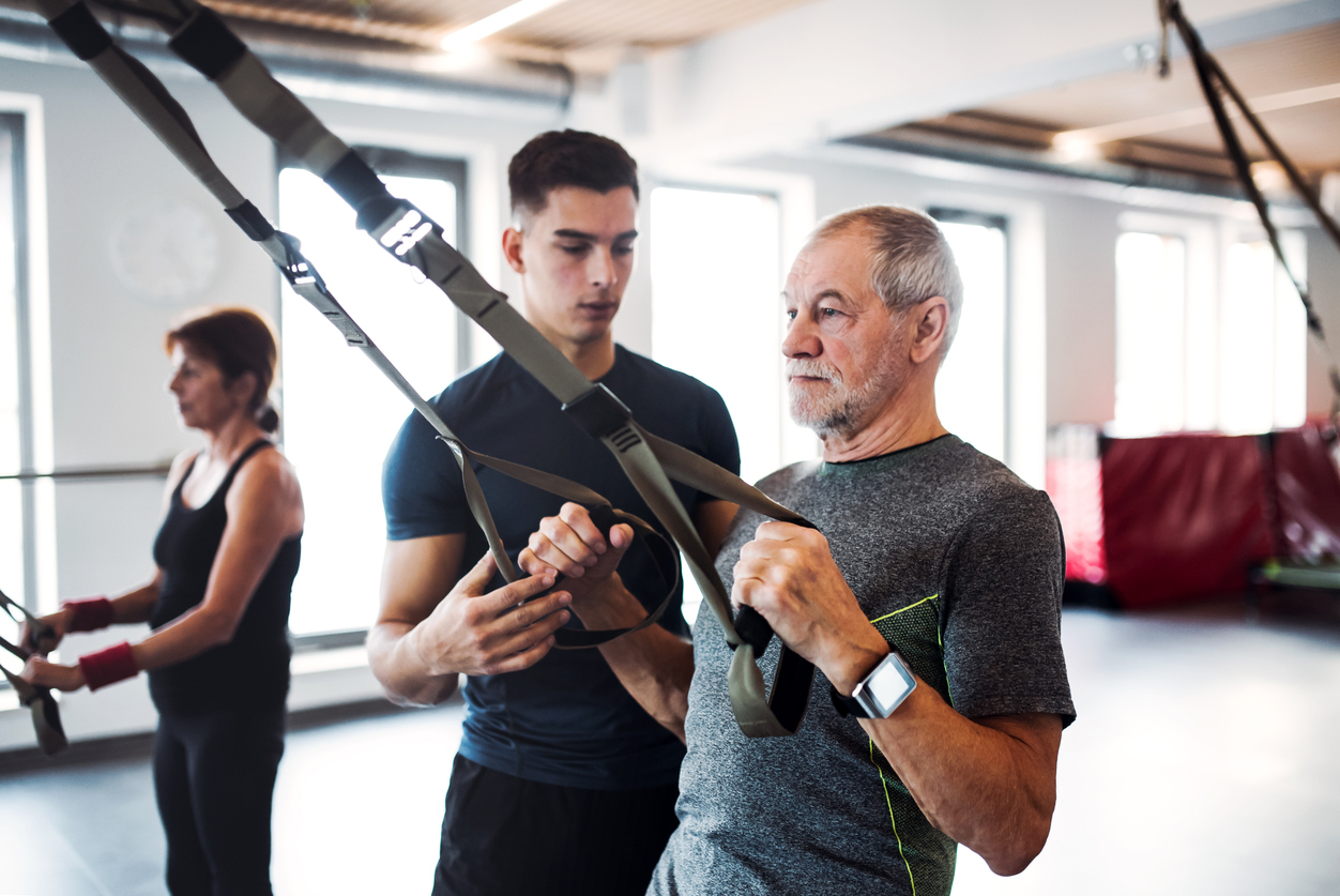 A group of seniors follow instructions from young trainer on an exercise with TRX bands.
