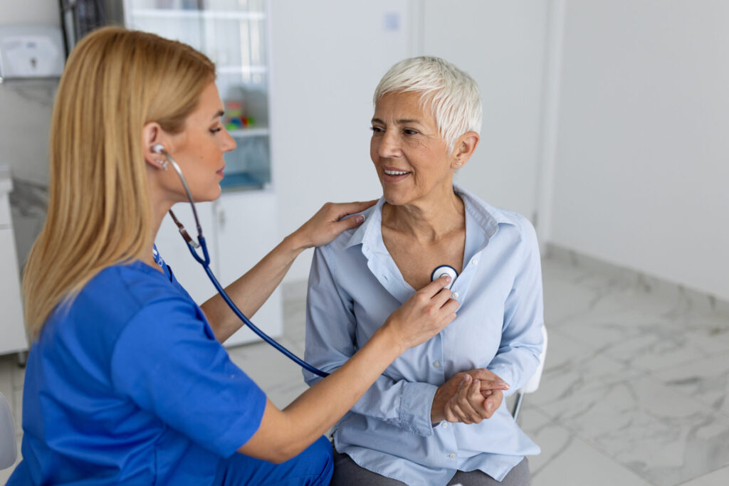 Adult female nurse listening to the heartbeat of elderly female patient.