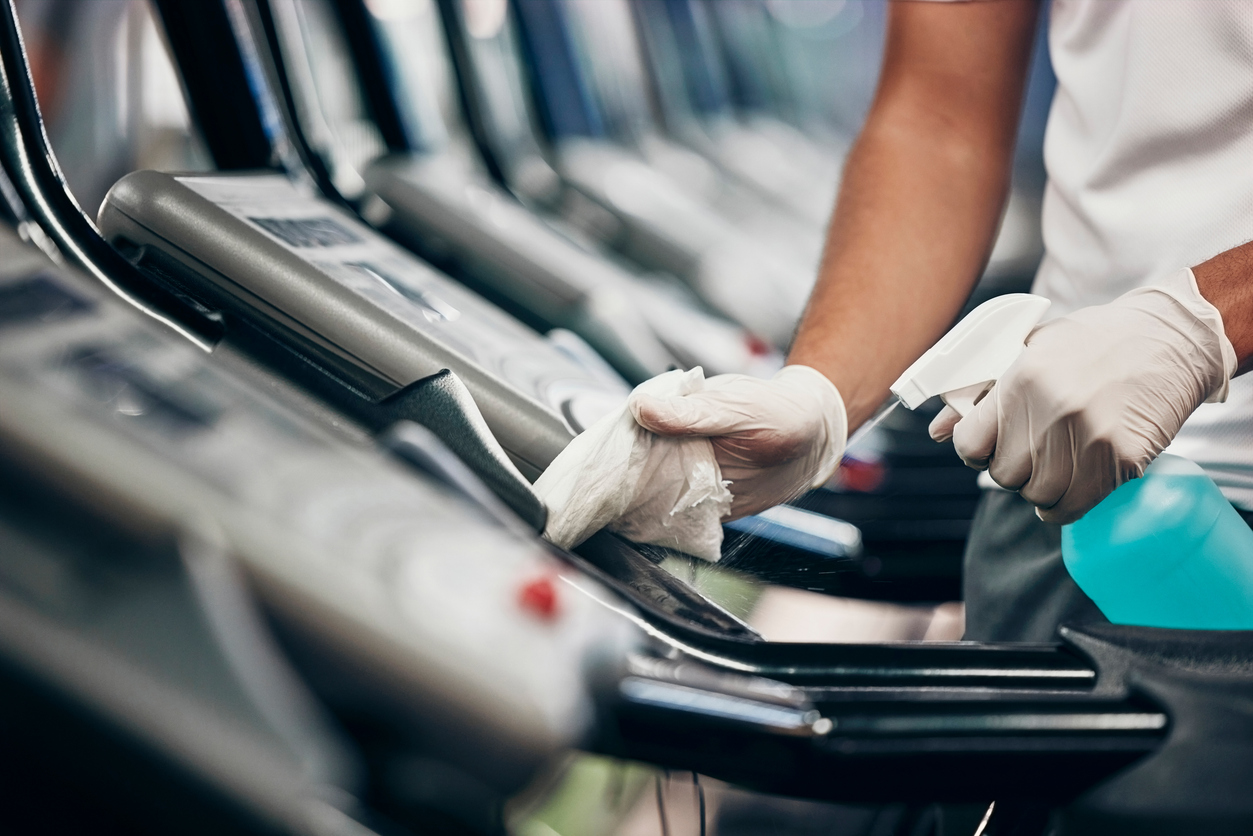 Closeup of a housekeeper cleaning and sanitizing a treadmill at a fitness center.