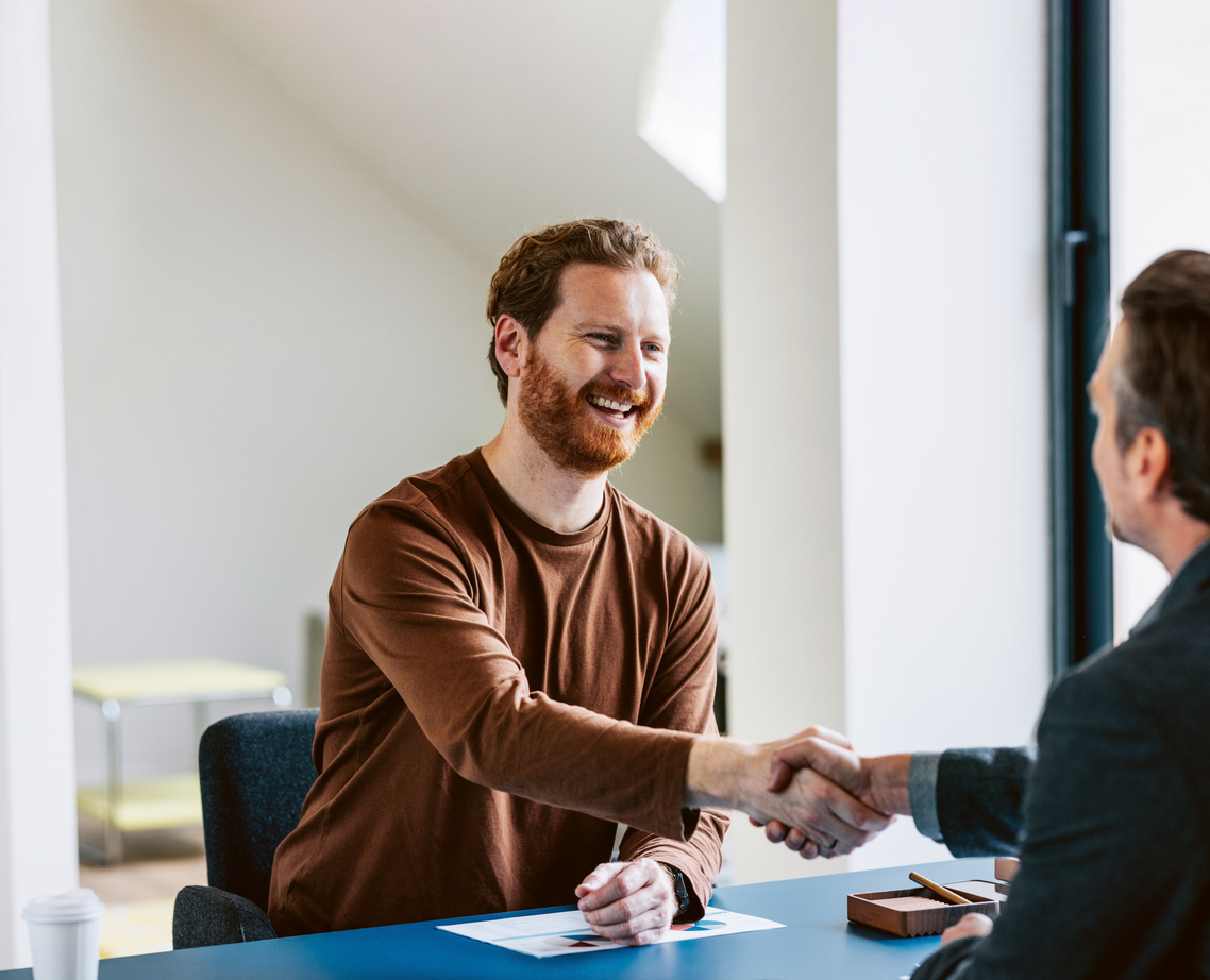 Cheerful bearded man shaking hands with interviewer in a bright office setting.
