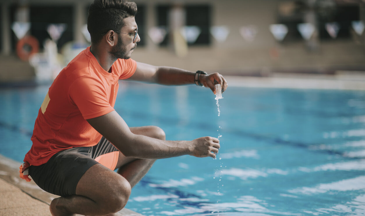 A male lifeguard checks a pool's chlorine level with a testing kit.