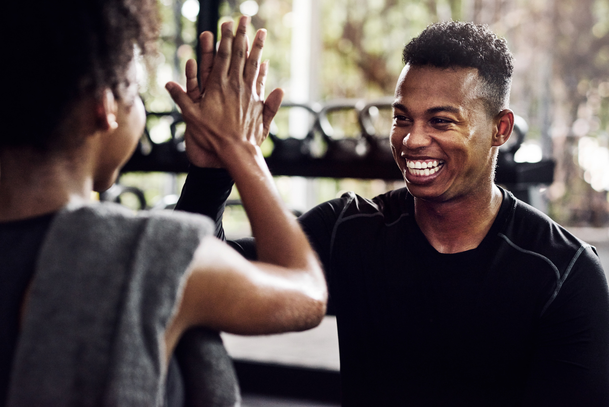 A young male fitness instructor gives his client a high five at the gym.
