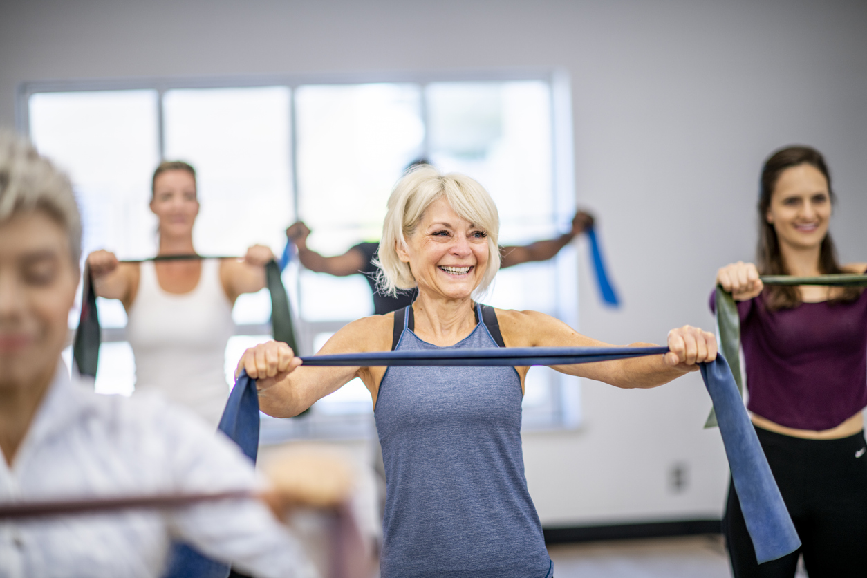 An elderly woman smiles as she works out with a resistance band during a fitness class.