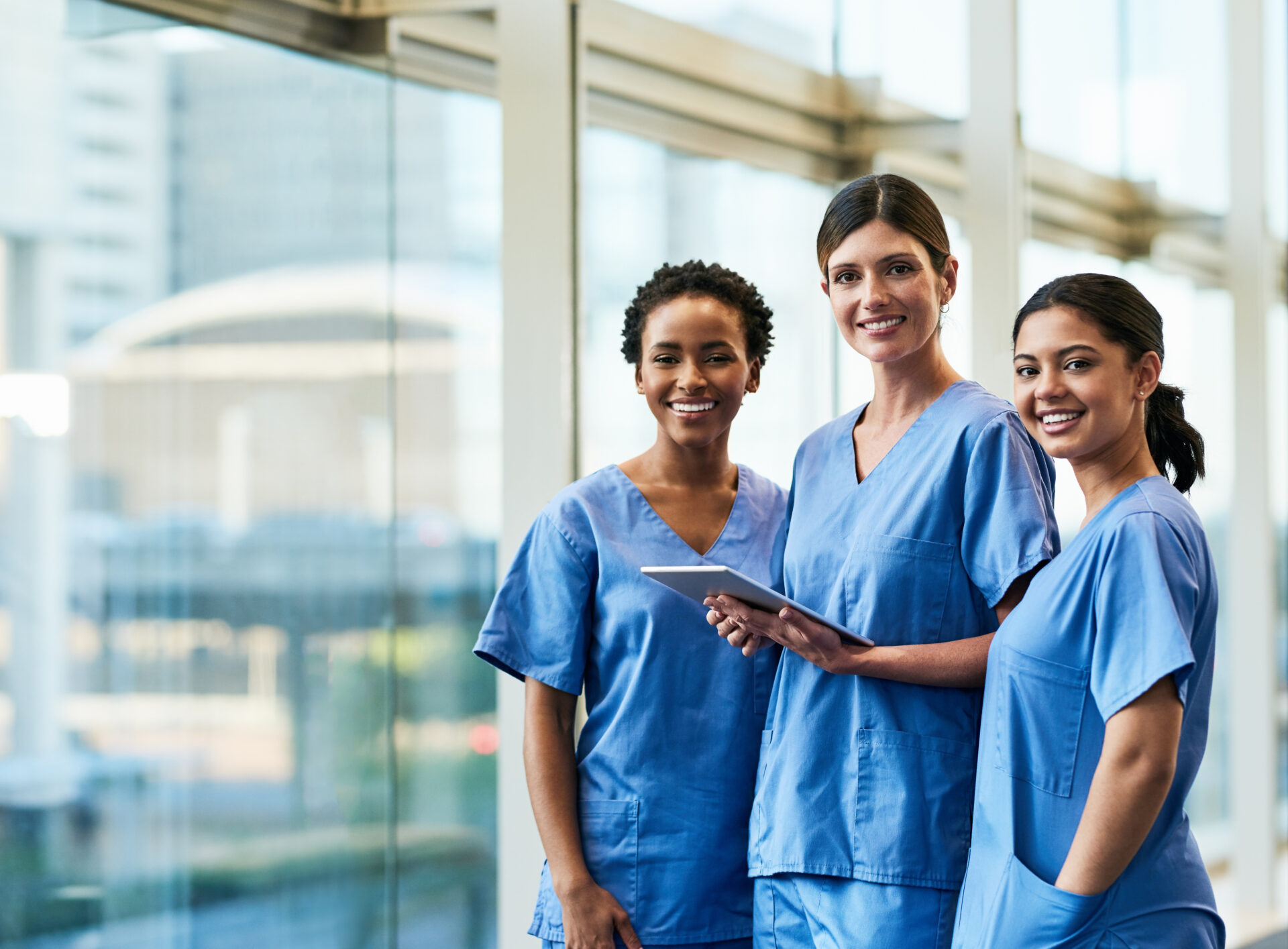 Group of three female nurses in scrubs smiling.