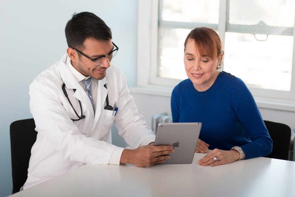 Adult male physician reviews medical records on a tablet with adult female patient.