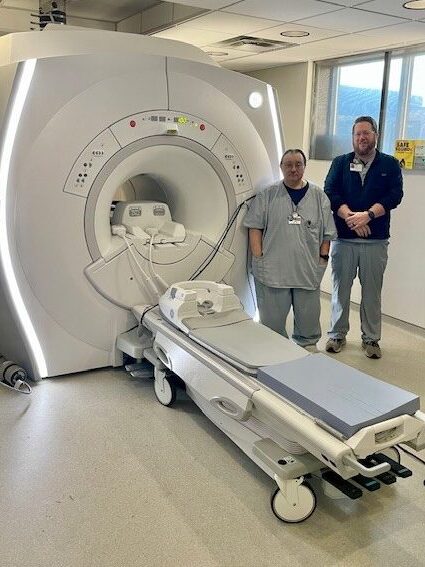 Two male staff member standing next to new imaging equipment at Claiborne Medical Center.