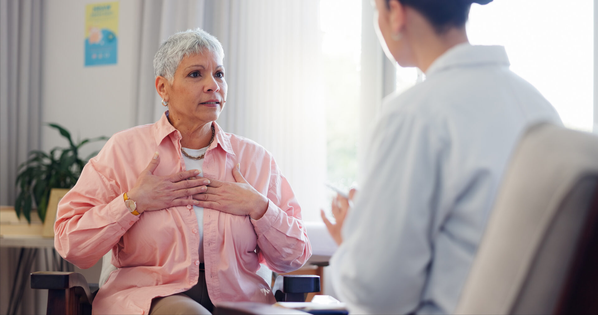 A doctor provides a heart consultation with elderly woman who has her hands over her heart.
