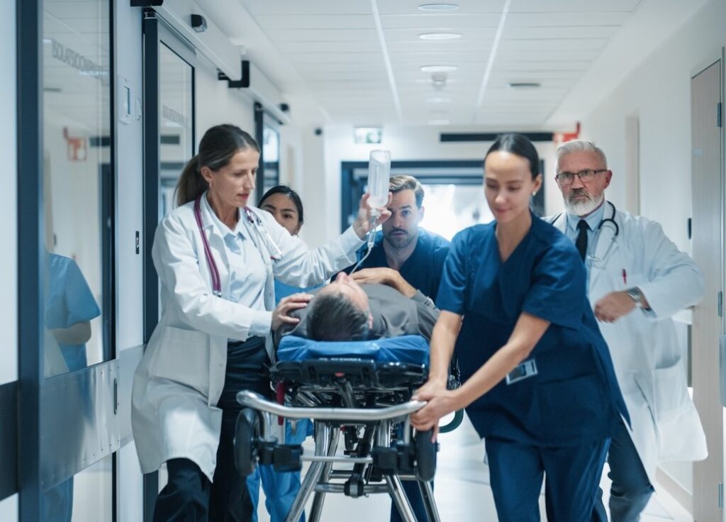 Five hospital emergency team members bring a patient on a stretcher down a hallway.