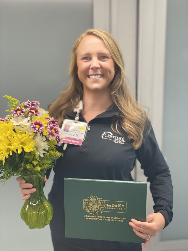 Smiling nurse holding bouquet of daisies and DAISY Award certificate.