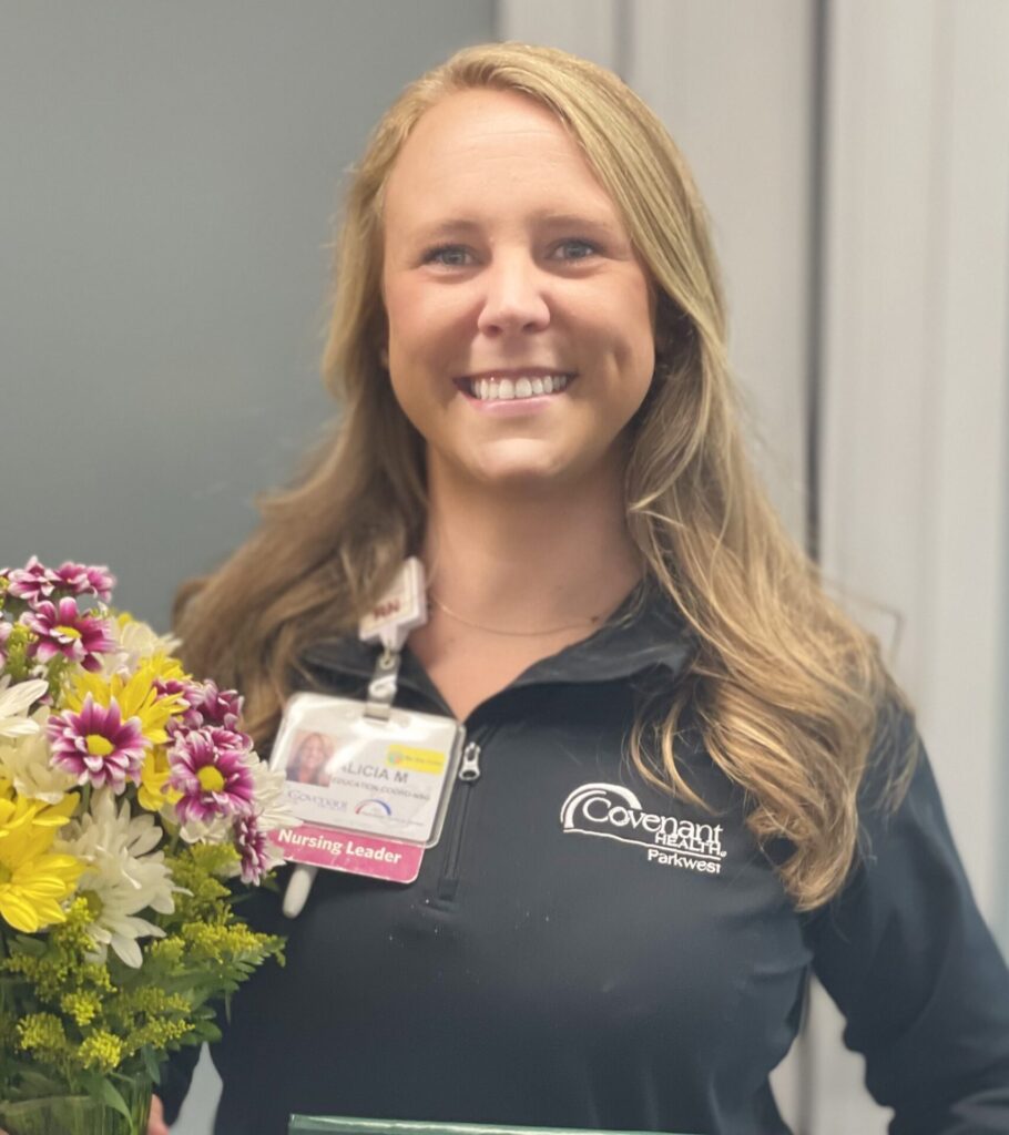 Smiling blonde nurse in black top holding bouquet of daisies.